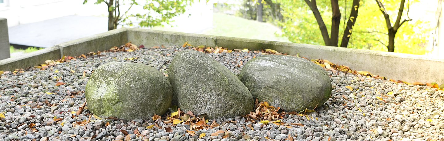 Tre stenar på rad på mark av grus.