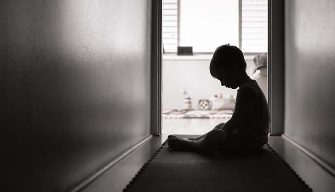 ensam ledsen pojke i korridor med lekrum i bakgrunden, svartvitt foto. 